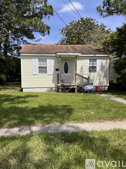 A small house with a porch and a tree in front.