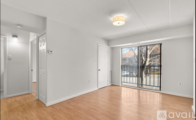 A room with wooden floors and white walls, with a window showing a view of a tree and a building outside.