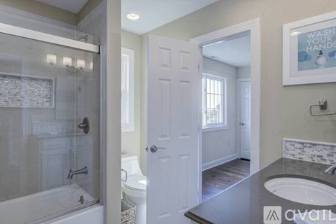 A bathroom with a glass shower stall, a white toilet, a white door, and a sink with a marble countertop.