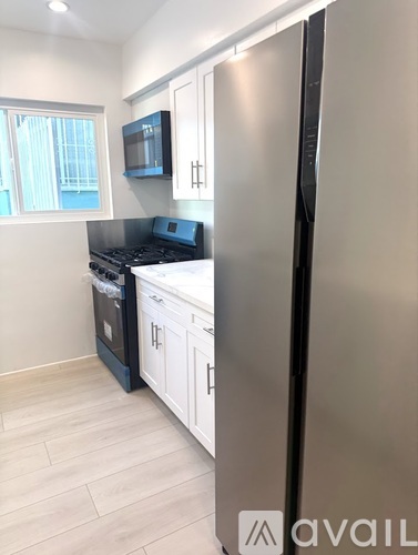 A kitchen with a stainless steel refrigerator, black stove, and white cabinets.