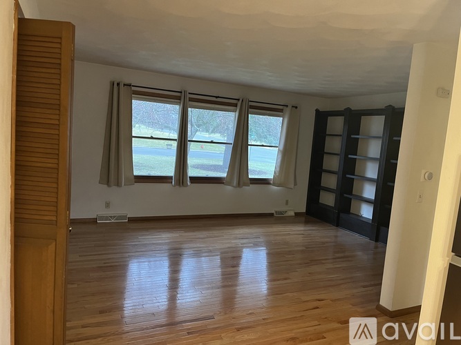 A room with wooden floors and a large window with a view of a lawn and trees.
