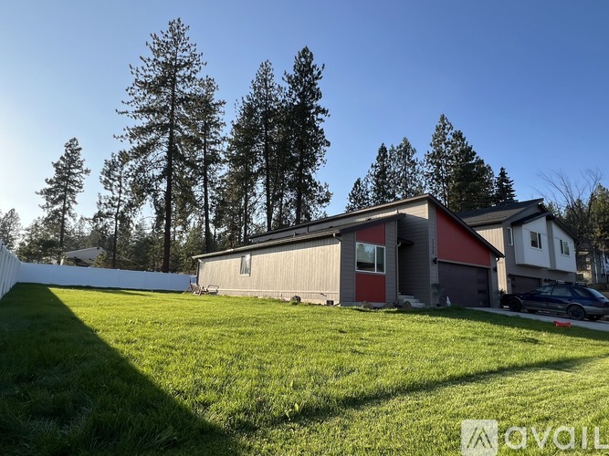 A house with a red roof is surrounded by a white fence and green grass.