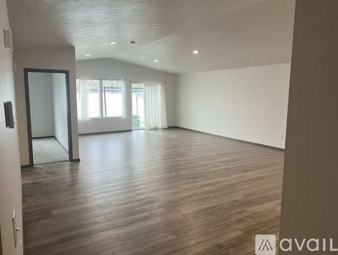 A spacious room with wooden flooring and a sliding glass door leading to a balcony.