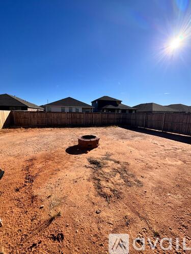 A dirt field with a fence and buildings in the background.