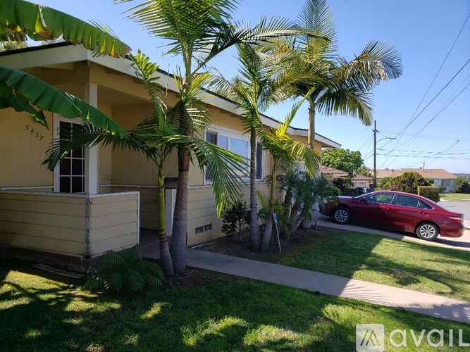 A red car is parked in front of a house with a palm tree.