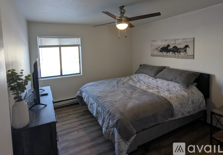 A bedroom with a bed, a ceiling fan, and a painting on the wall.