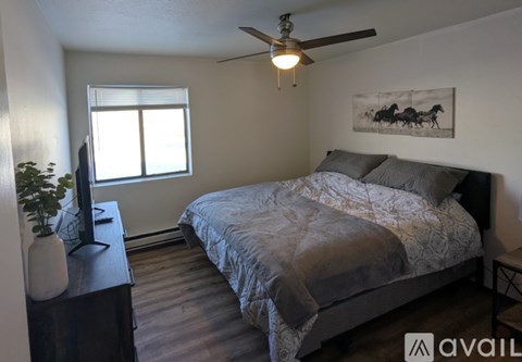 A bedroom with a bed, a ceiling fan, and a painting on the wall.