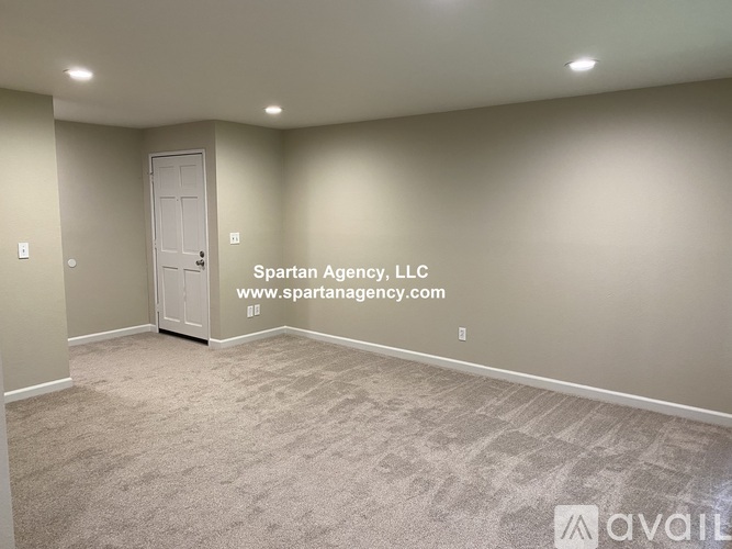 A room with a carpeted floor and a door, with a Spartan Agency logo and website on the wall.
