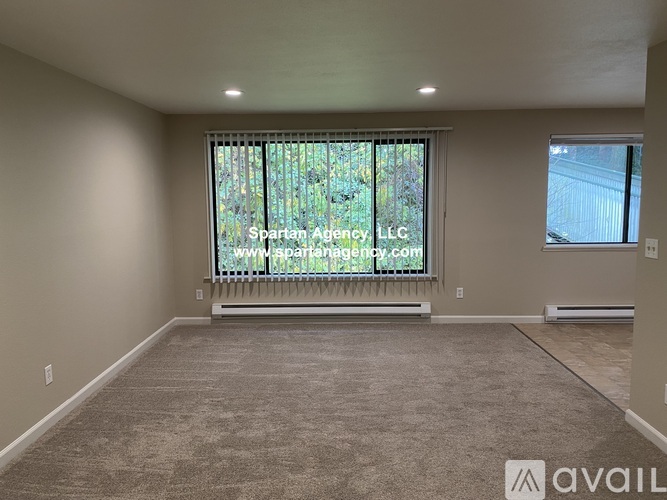 A spartan empty room with carpeted floor and a window with blinds.