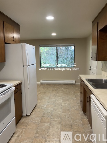 A kitchen with a white refrigerator and a window with a view of trees outside.