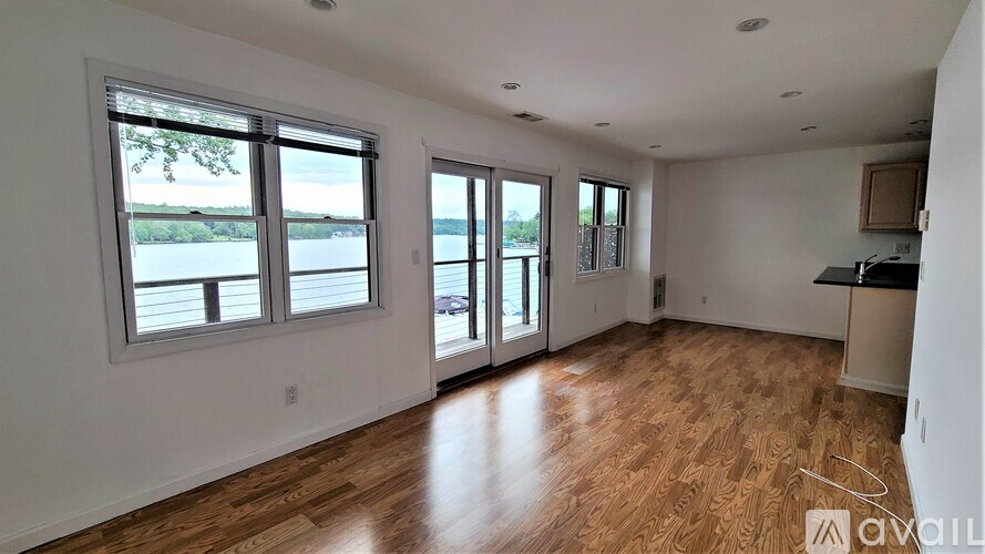 A spacious room with wooden flooring and large windows overlooking a body of water.