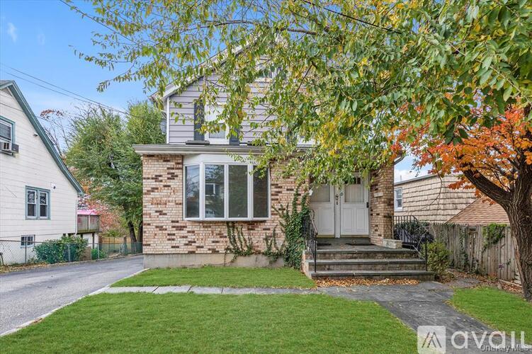 A house with a white door and a brick wall is surrounded by a green lawn.