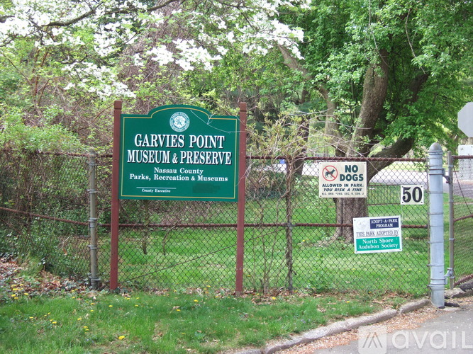 A two-story house with a garage is surrounded by a fence and trees.