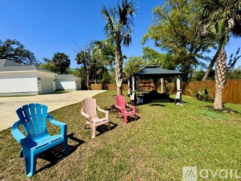 A blue chair sits in the foreground of a yard with a gazebo and palm trees.