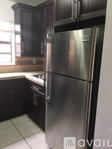 A stainless steel refrigerator stands in a kitchen with dark wood cabinets.