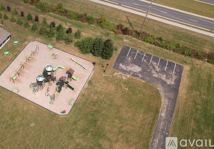 A playground with a green and white slide and a parking lot.