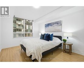 A bedroom with a large bed, a small table with a plant, and a picture on the wall.