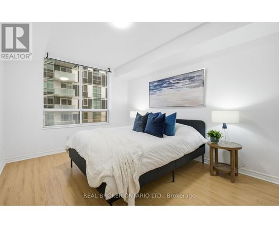 A bedroom with a large bed, a small table with a plant, and a picture on the wall.