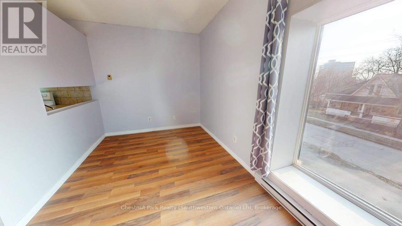 A room with wooden flooring and a window showing a view of a residential area.