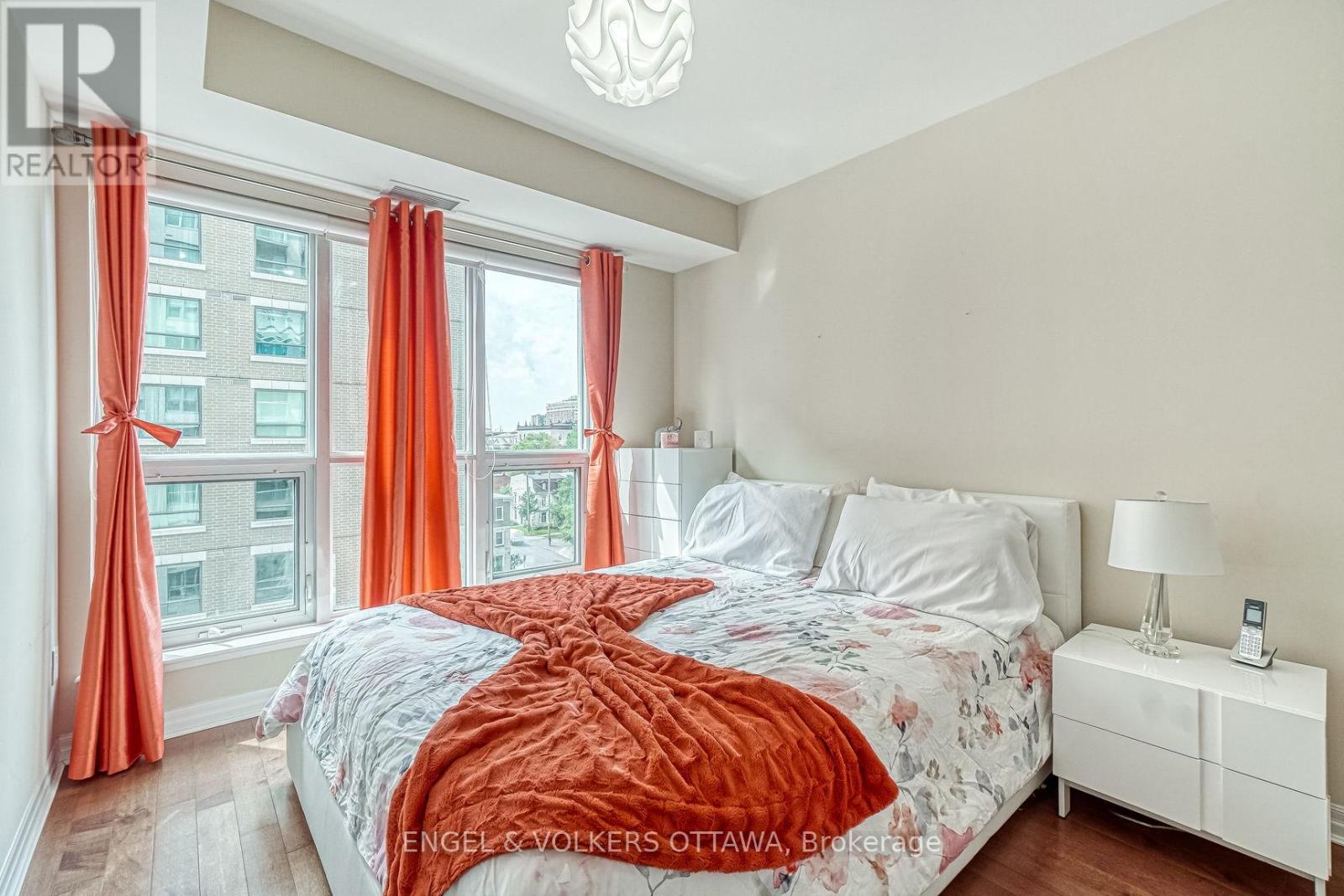A bedroom with a large bed and a window with orange curtains.