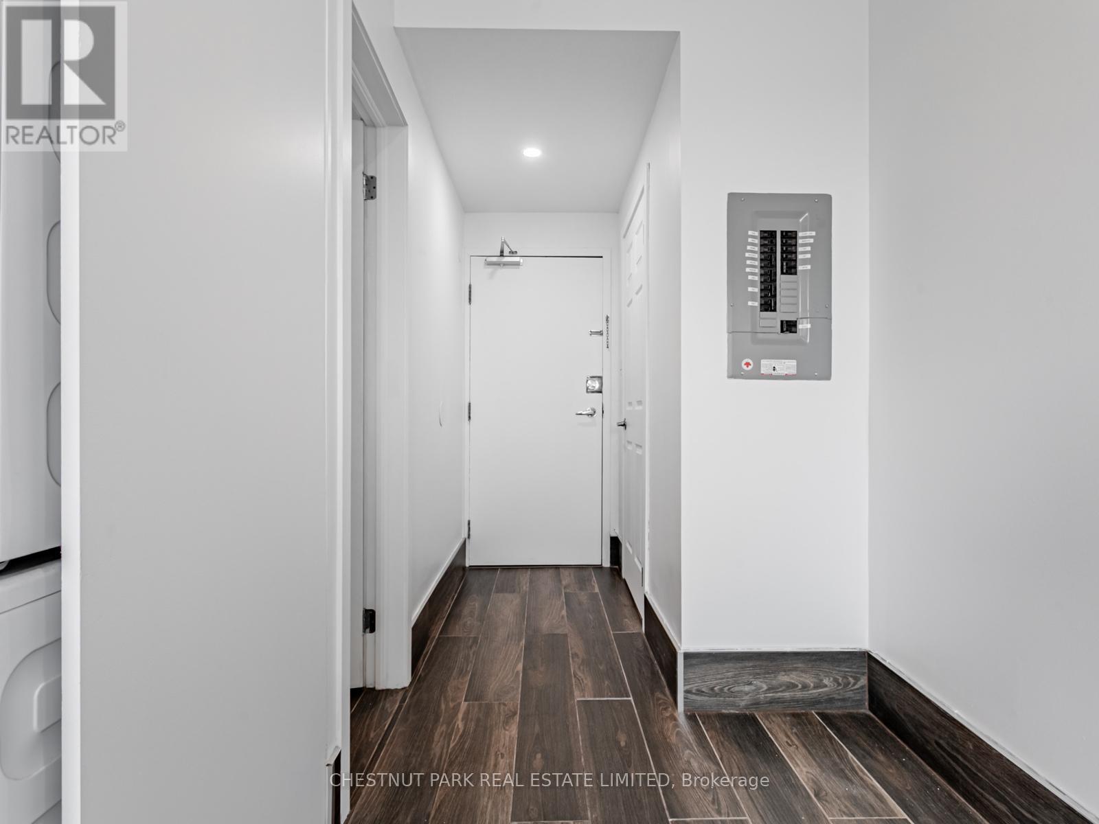 A hallway with a washer and dryer on the left and a control panel on the wall.