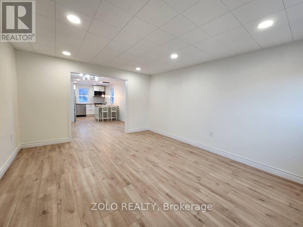 A spacious room with wooden flooring and white walls, with a desk and chairs in the corner.