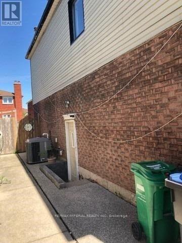 A green trash bin sits on a concrete surface next to a brick wall.