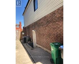 A green trash bin sits on a concrete surface next to a brick wall.