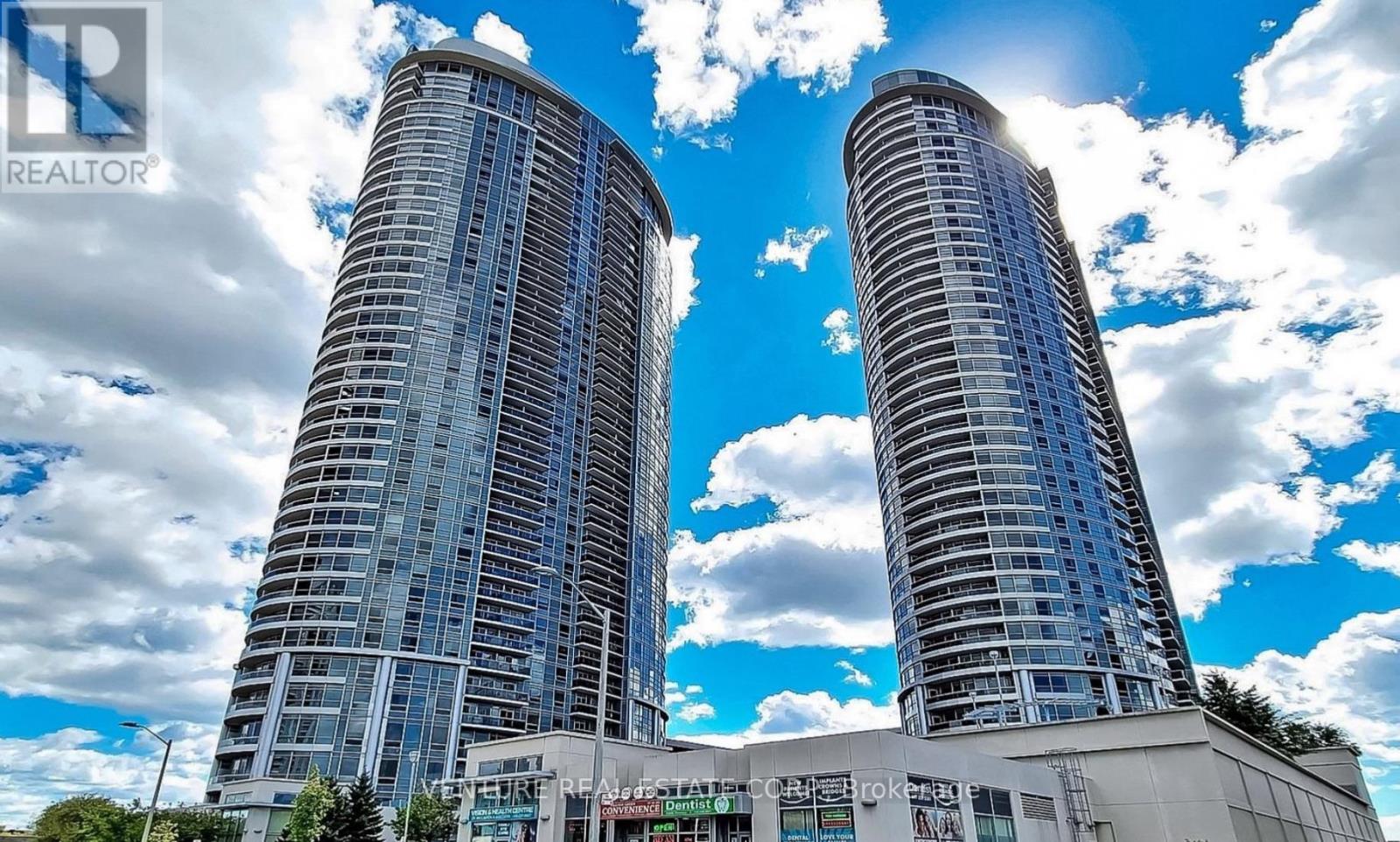Two tall buildings with glass windows and a blue sky with clouds in the background.