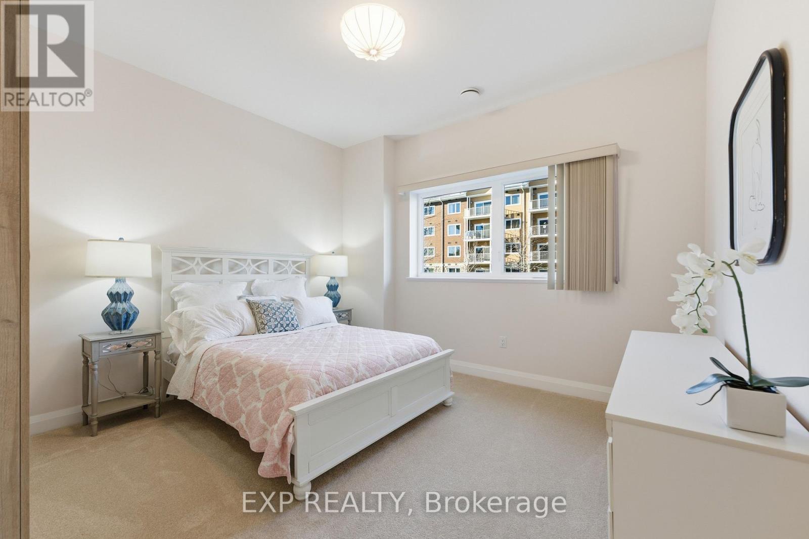 A bedroom with a bed, nightstand, and a window with a view of a building.