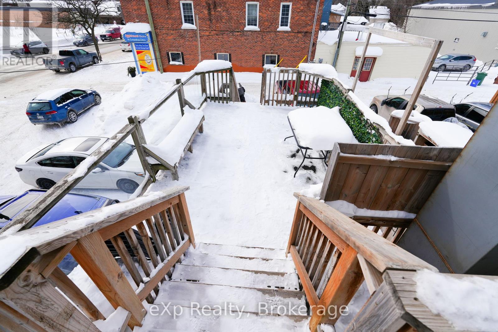A snow-covered deck with a railing and steps leading to a building.