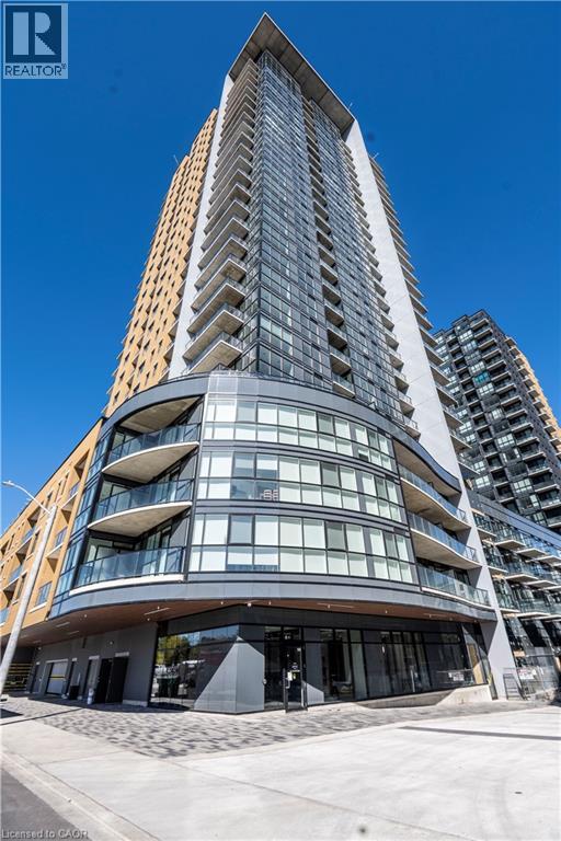 A tall, modern building with a curved glass facade stands in front of a clear blue sky.
