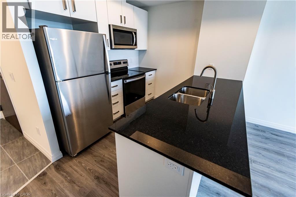 A modern kitchen with a stainless steel refrigerator and black countertops.