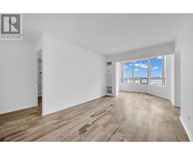 A room with white walls and wooden flooring, with a window showing a blue sky with clouds.