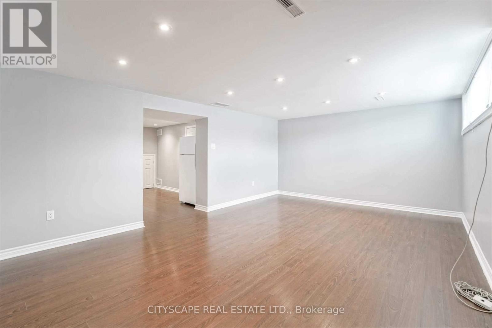A spacious room with wooden flooring and white walls.