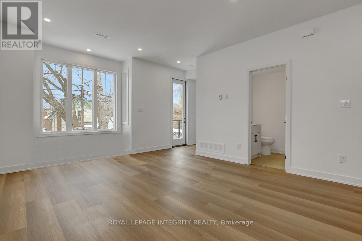 A spacious room with wooden flooring and white walls, with a window showing a tree outside.