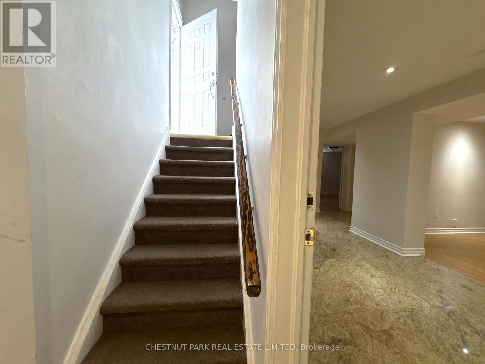 A staircase with a brown carpeted runner and wooden banister leads to a doorway.
