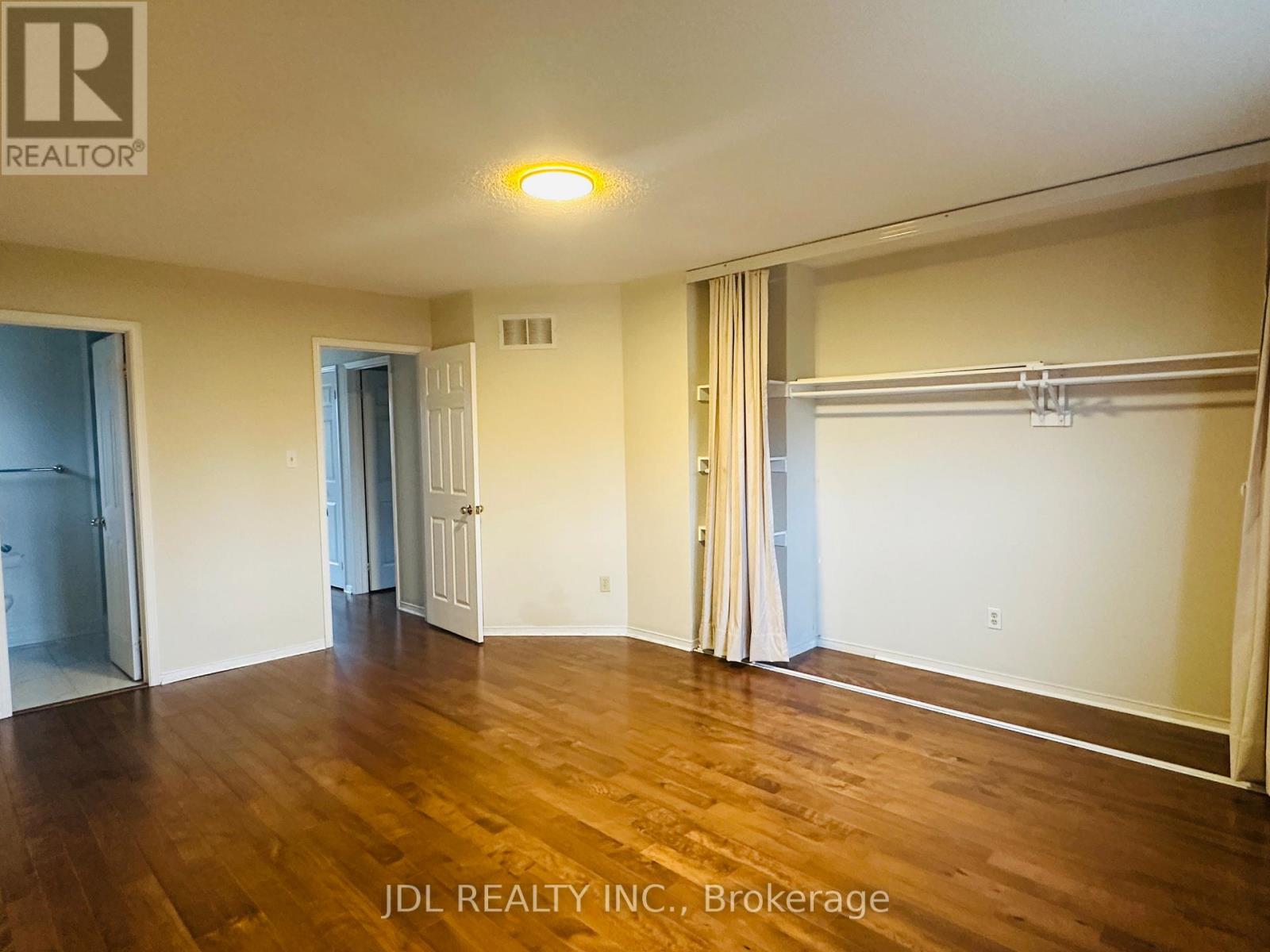 A spacious room with wooden floors and white walls, featuring a sliding door and a closet with a coat rack.