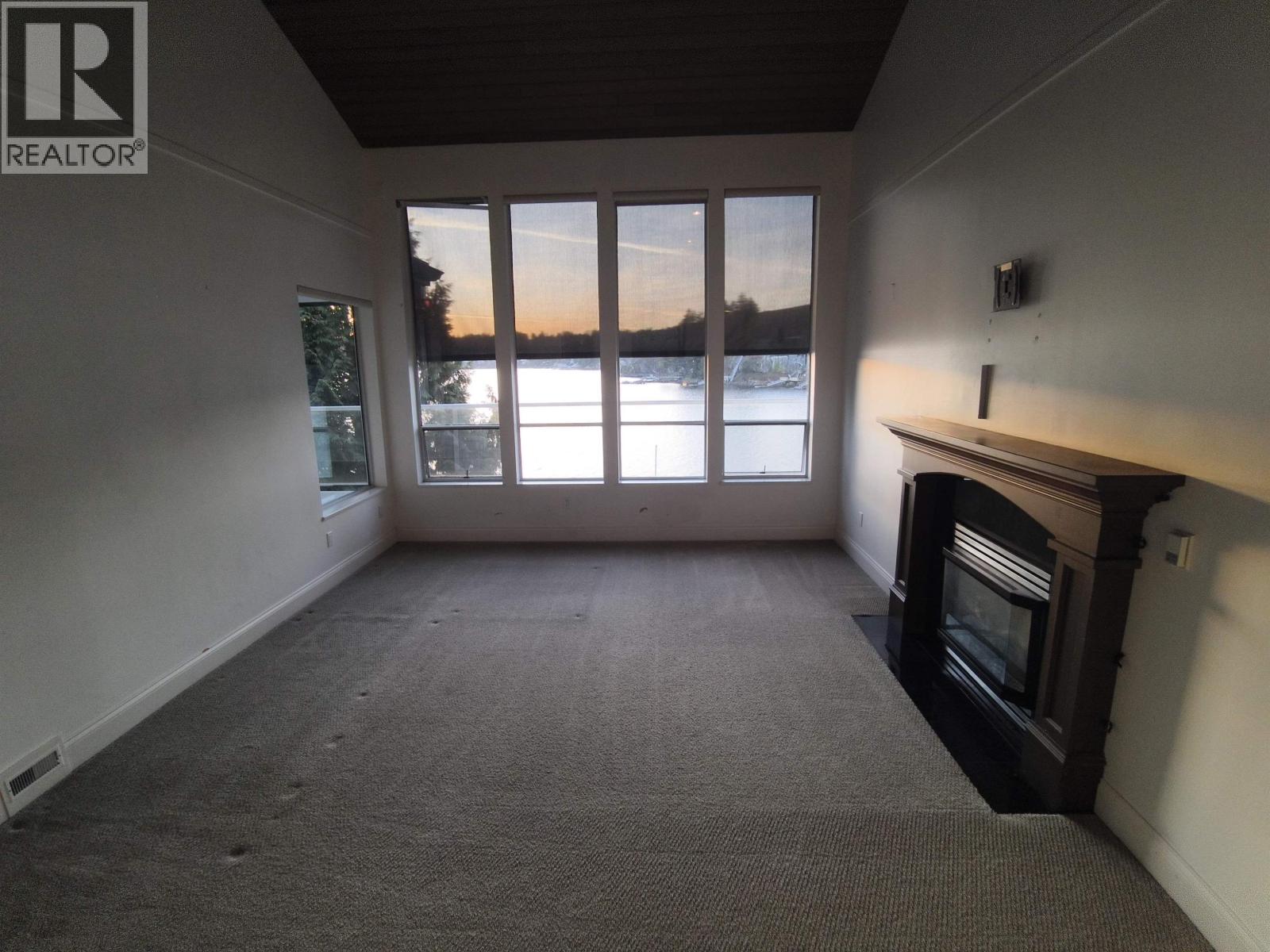 A large empty room with a fireplace and a window overlooking a body of water.