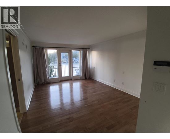 A room with wooden floors and a large window with curtains.