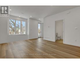 A spacious room with wooden flooring and white walls, with a window showing a tree outside.