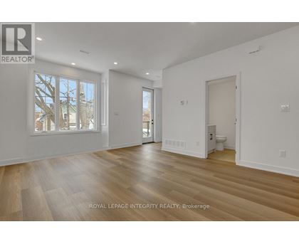 A spacious room with wooden flooring and white walls, with a window showing a tree outside.