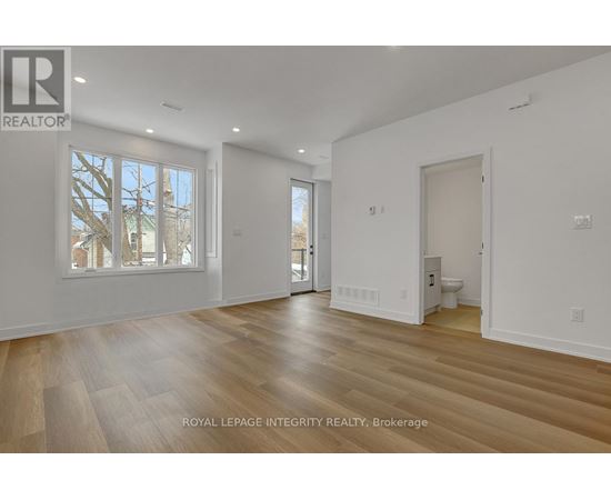 A spacious room with wooden flooring and white walls, with a window showing a tree outside.