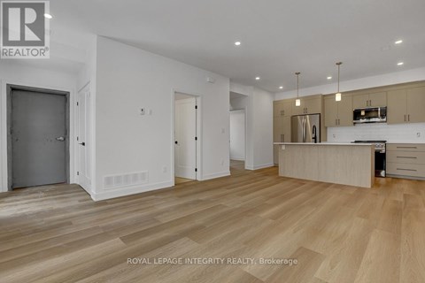A spacious room with wooden flooring and a kitchen area with a stove top oven.