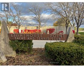 A sign for Lighthouse Point Yacht and Tennis Club sits in front of a fence and trees.
