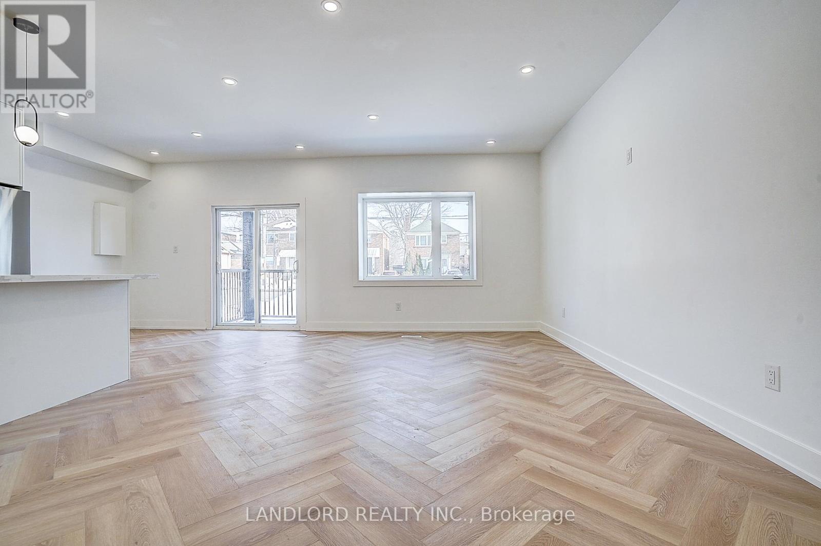 A spacious room with wooden flooring and two windows.