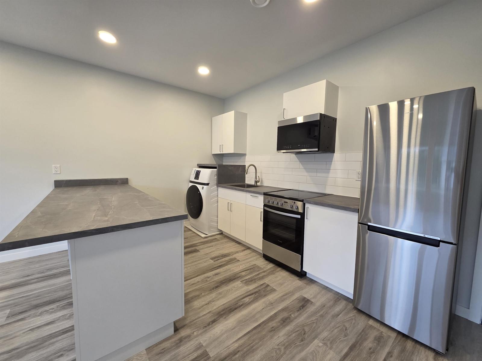 A modern kitchen with a stainless steel refrigerator, microwave, and oven.