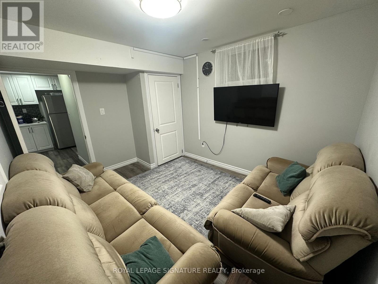 A living room with a couch, television, and a clock on the wall.