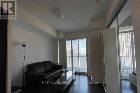 A black leather couch sits in a living room with a sliding glass door.