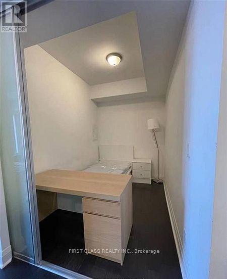 A small bedroom with a bed, nightstand, and desk.